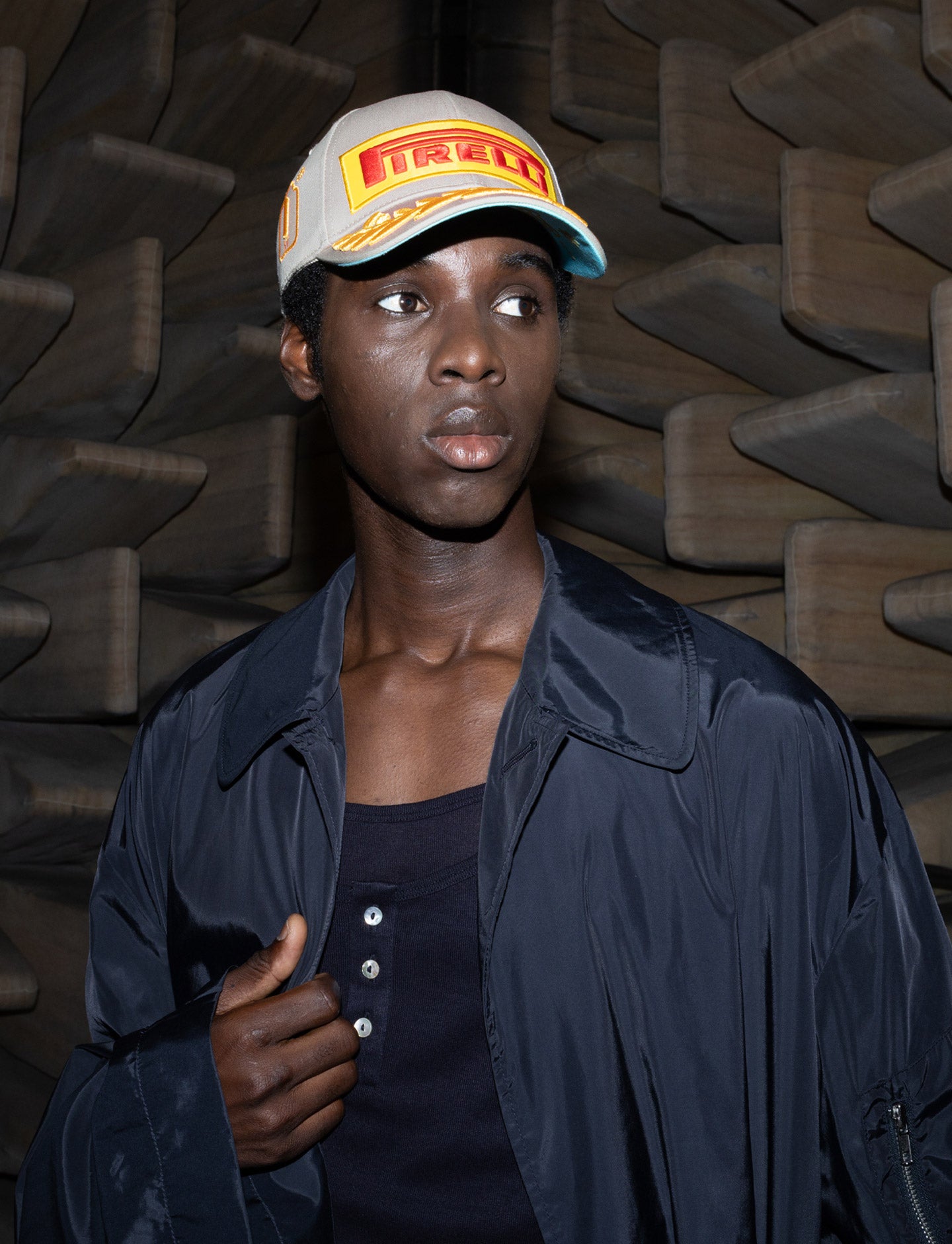 Person wearing a cap with a Pirelli logo against a textured dark sound room background