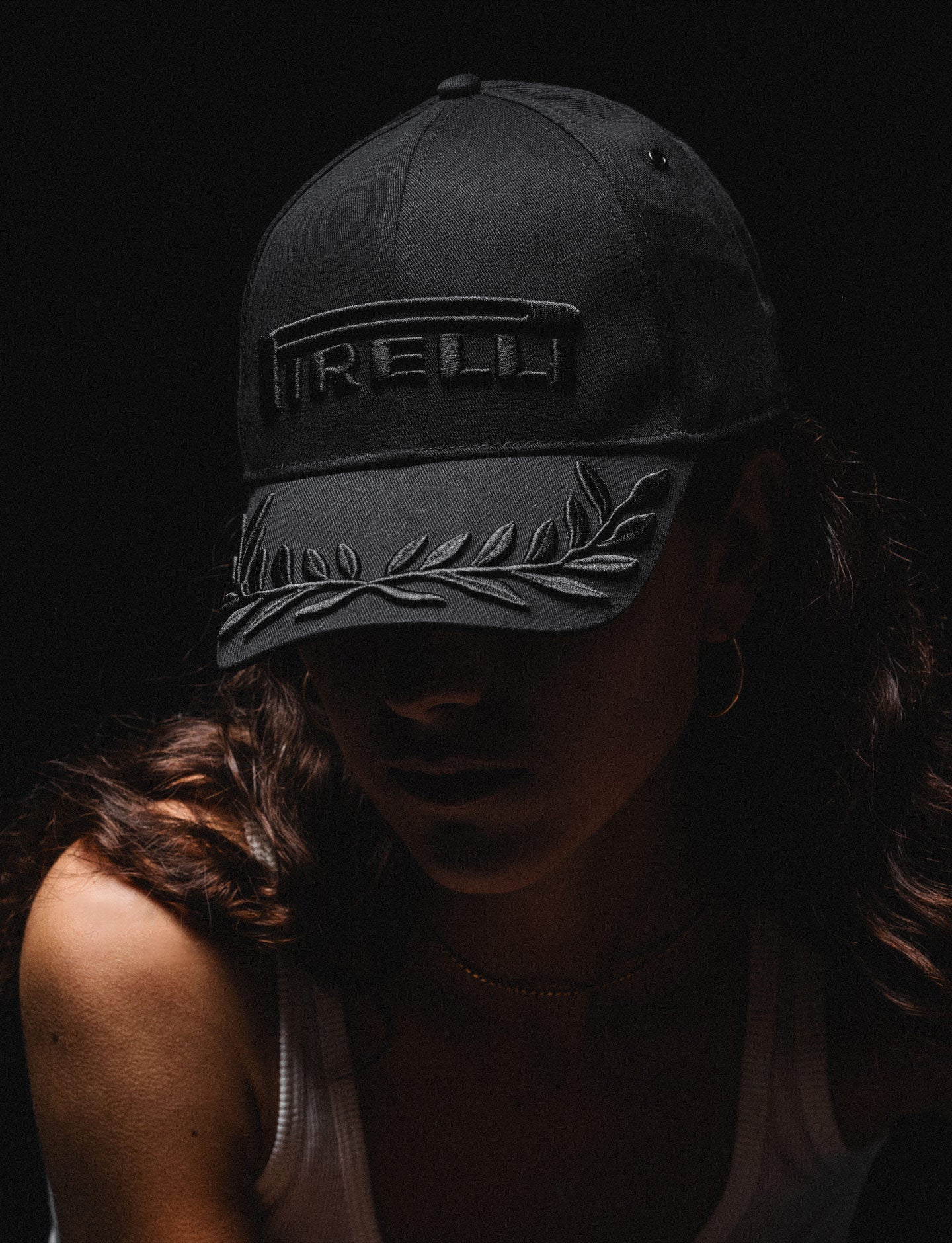 Person wearing a black-on-black cap with a Pirelli logo on a dark background