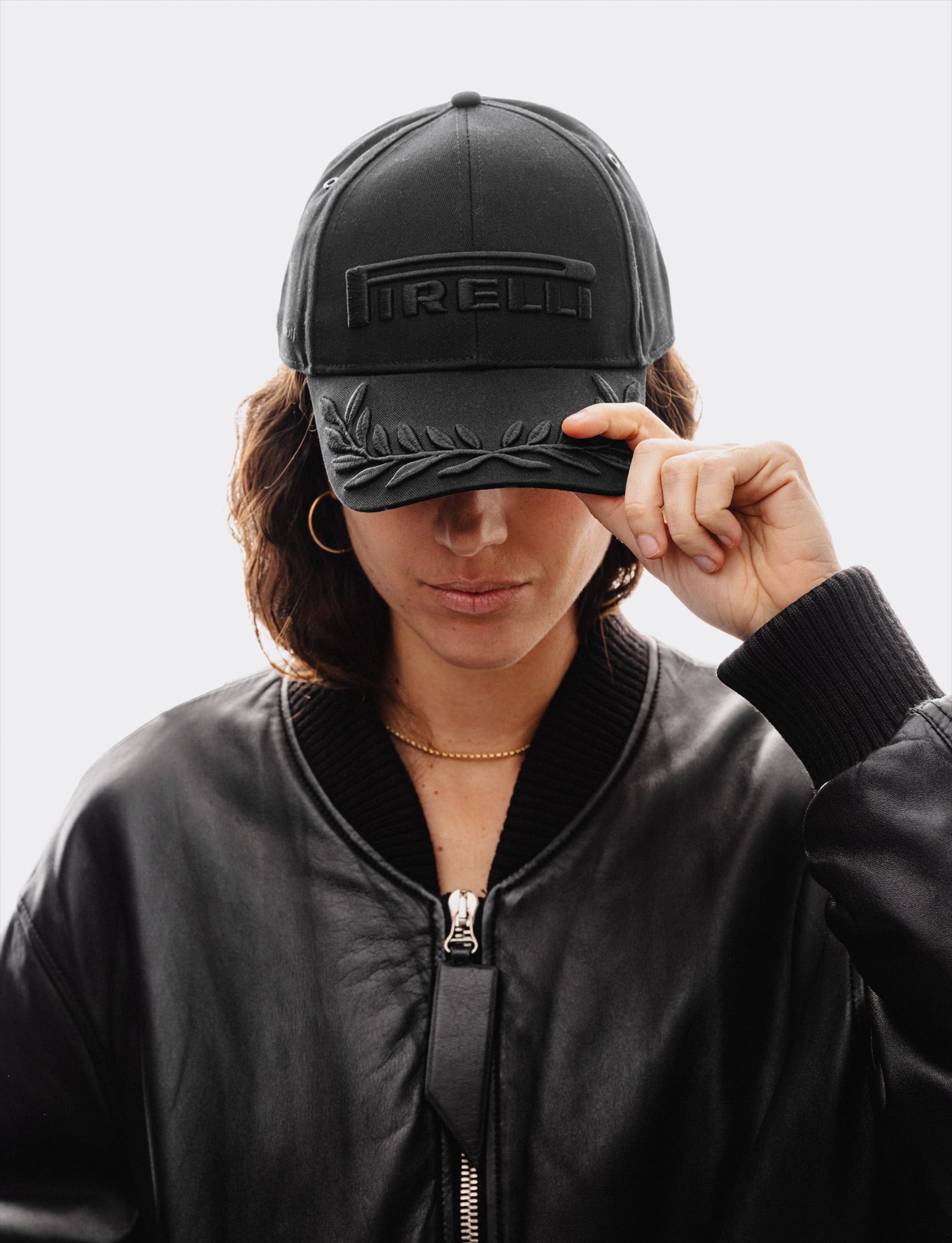 woman wearing a black on black Pirelli cap and a black leather jacket against a white background