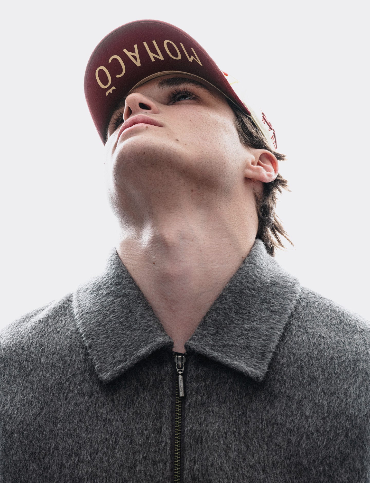 Person wearing a red cap with 'Monaco' text and a gray coat against a light background